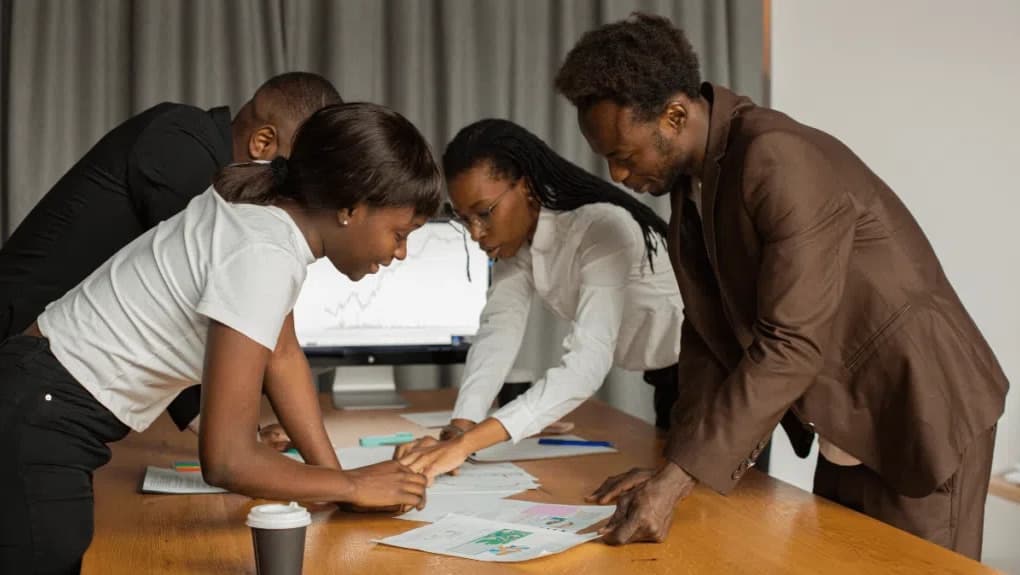 Four colleagues leaning over a table of charts and printouts, working through them together.