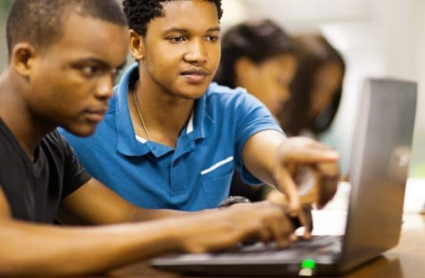 Two students at a laptop, one pointing something out on the screen to the other.
